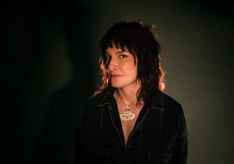 Australian singer-songwriter Jen Cloher posing for a moody press photo wearing a dark denim jacket and a pendant necklace.